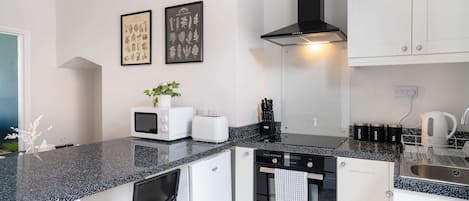 Una cocina moderna con armarios blancos, encimera negra, microondas, tostadora y pileta. Hay dos grabados botánicos enmarcados en la pared.