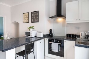 A modern kitchen with white cabinets, a black countertop, a microwave, a toaster, and a sink. There are two framed botanical prints on the wall. - Stylish House In Bishop Auckland Wifi Parking (Bishop Auckland)