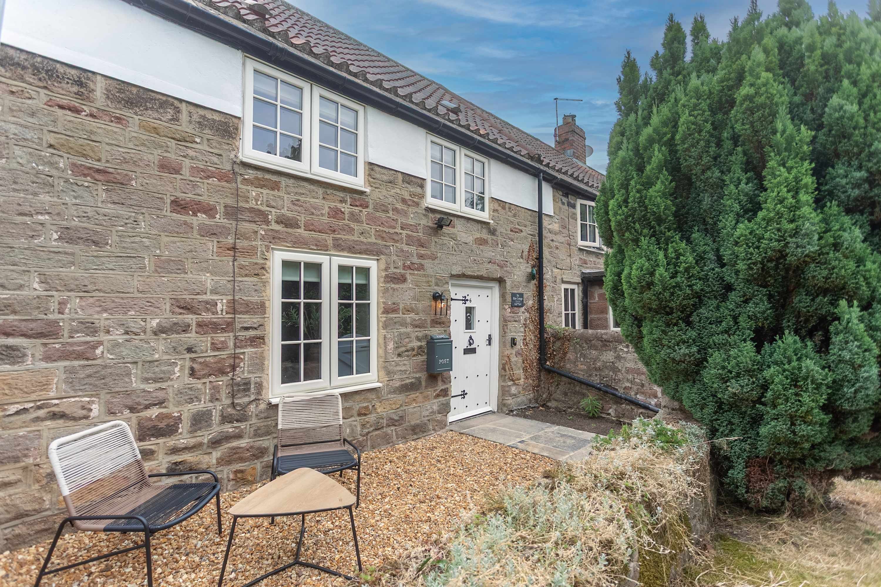 A stone house with a white door, a bench, and a table outside.
