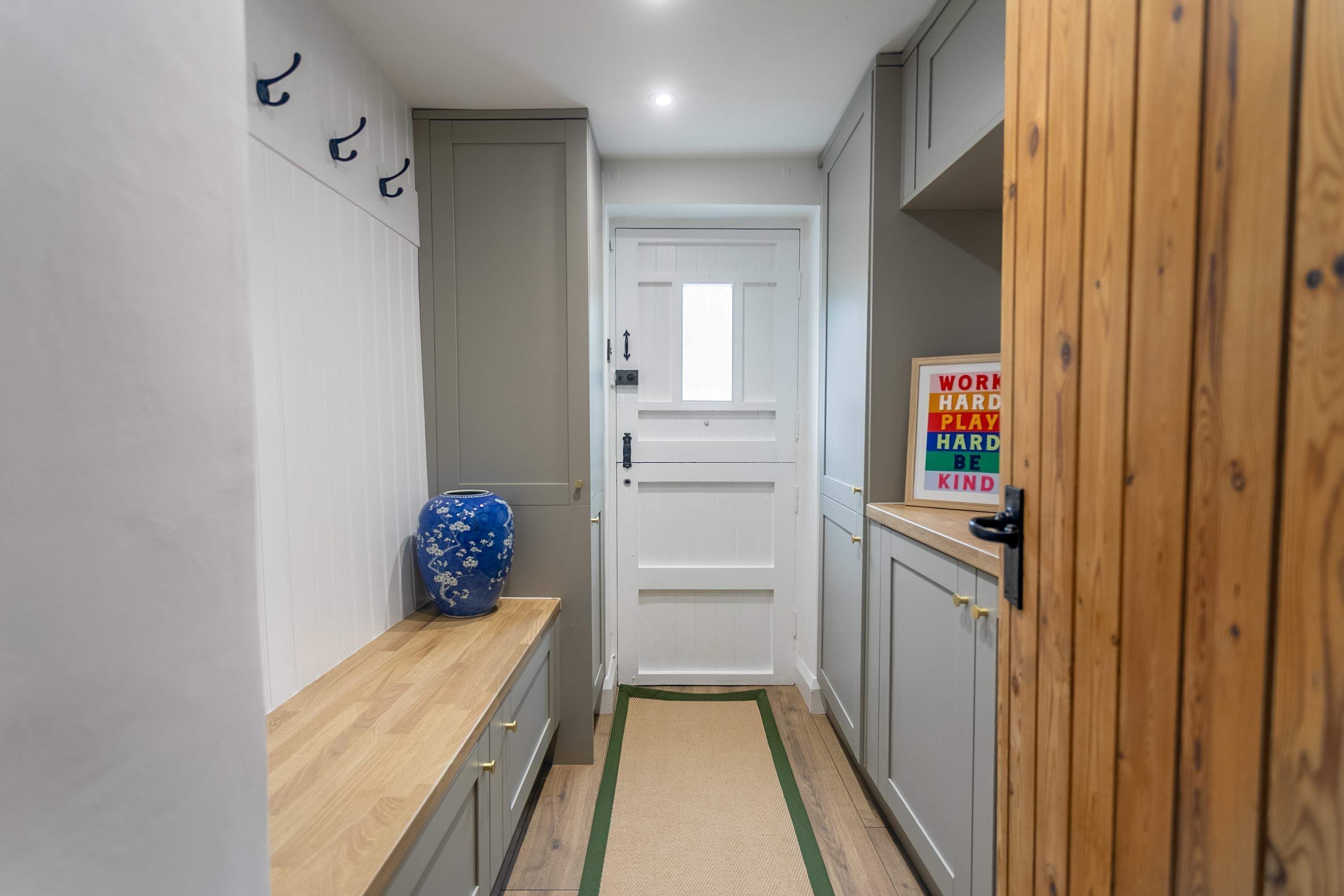 A narrow hallway with a wooden bench, a blue vase, and a motivational sign on the wall.