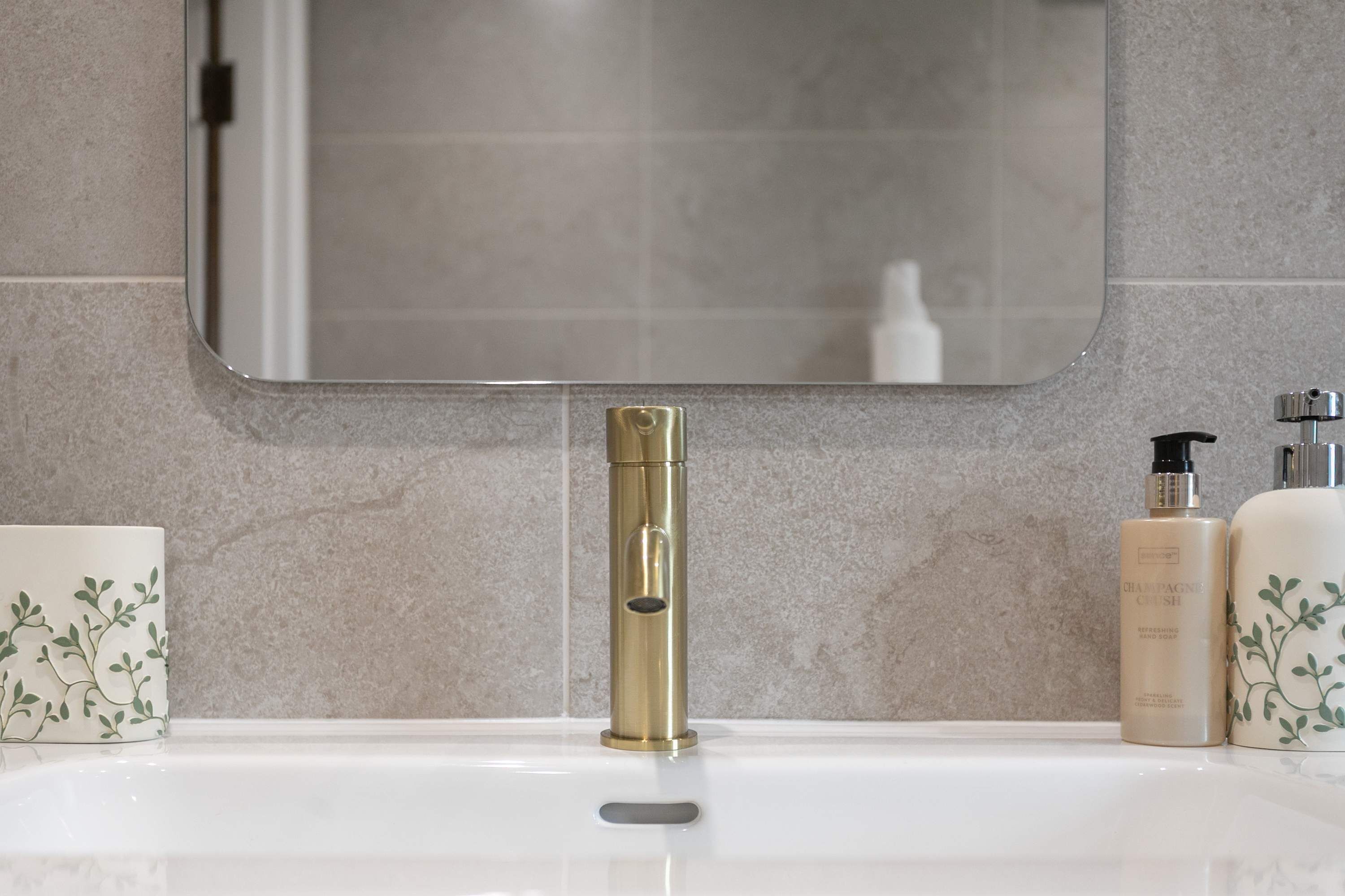 Un baño con un lavamanos blanco, un grifo dorado y dos jabones para manos.