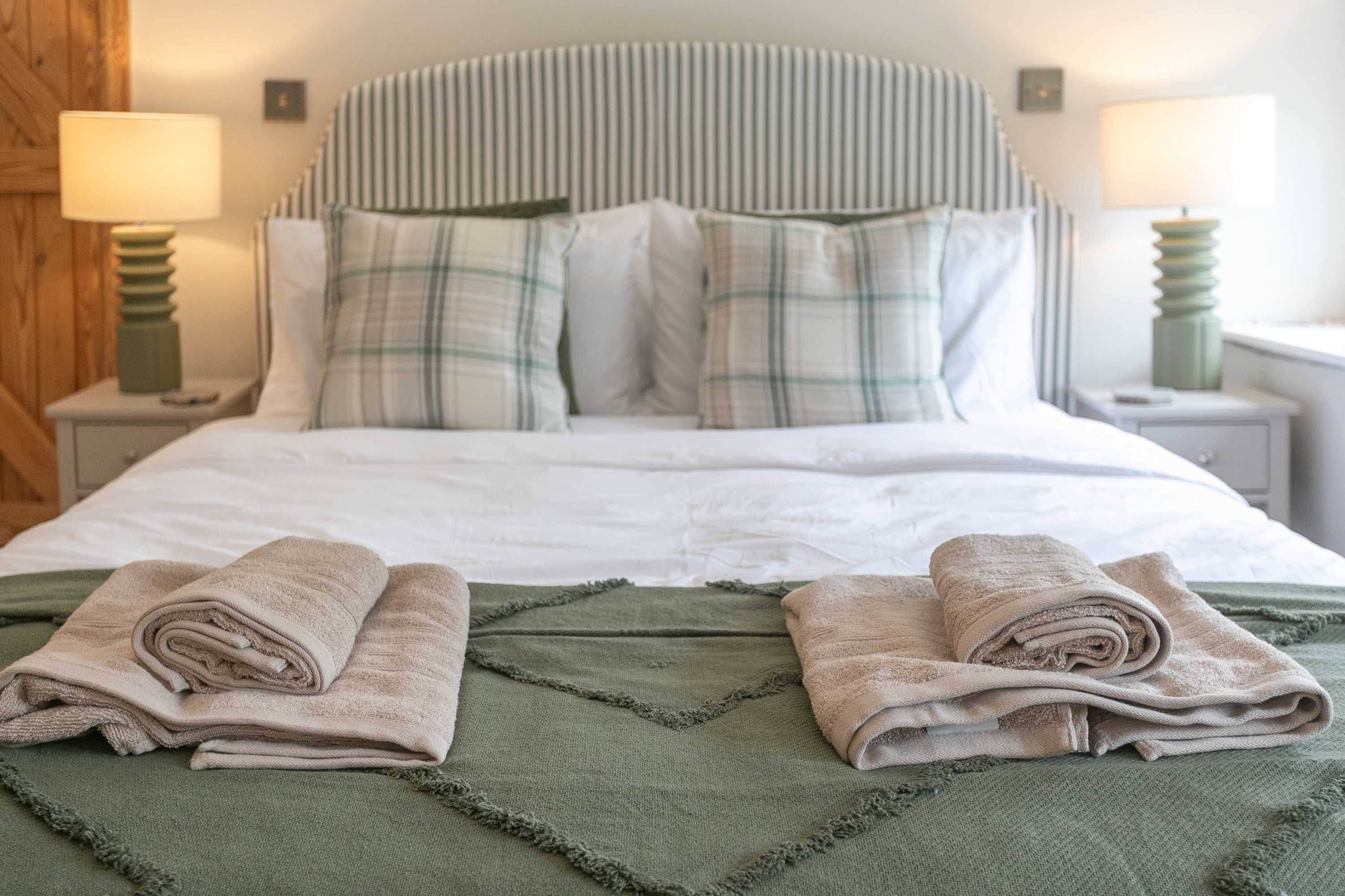 A neatly made bed with a striped headboard, two pillows, and two rolled towels on a green blanket.