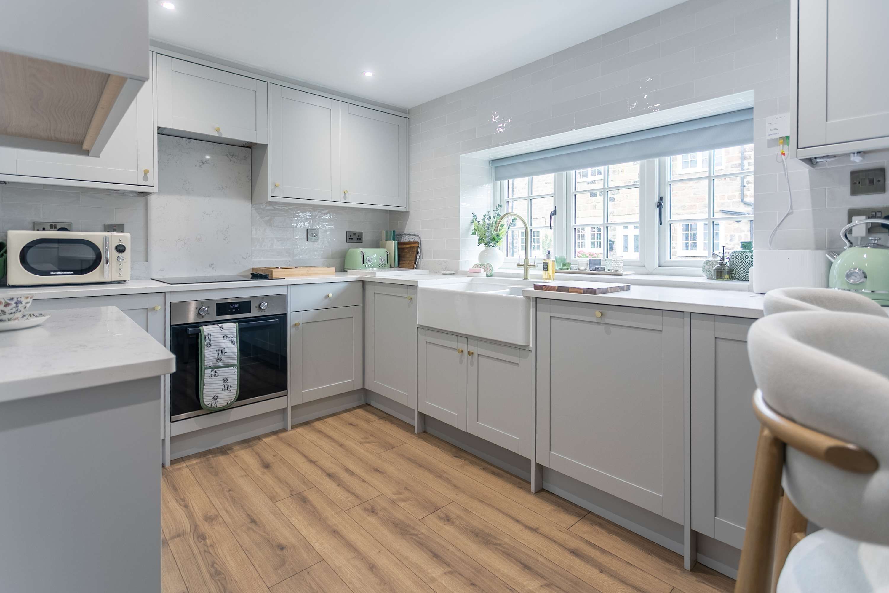 A modern kitchen with white cabinets, a built-in oven, a microwave, and a window with a view of buildings.