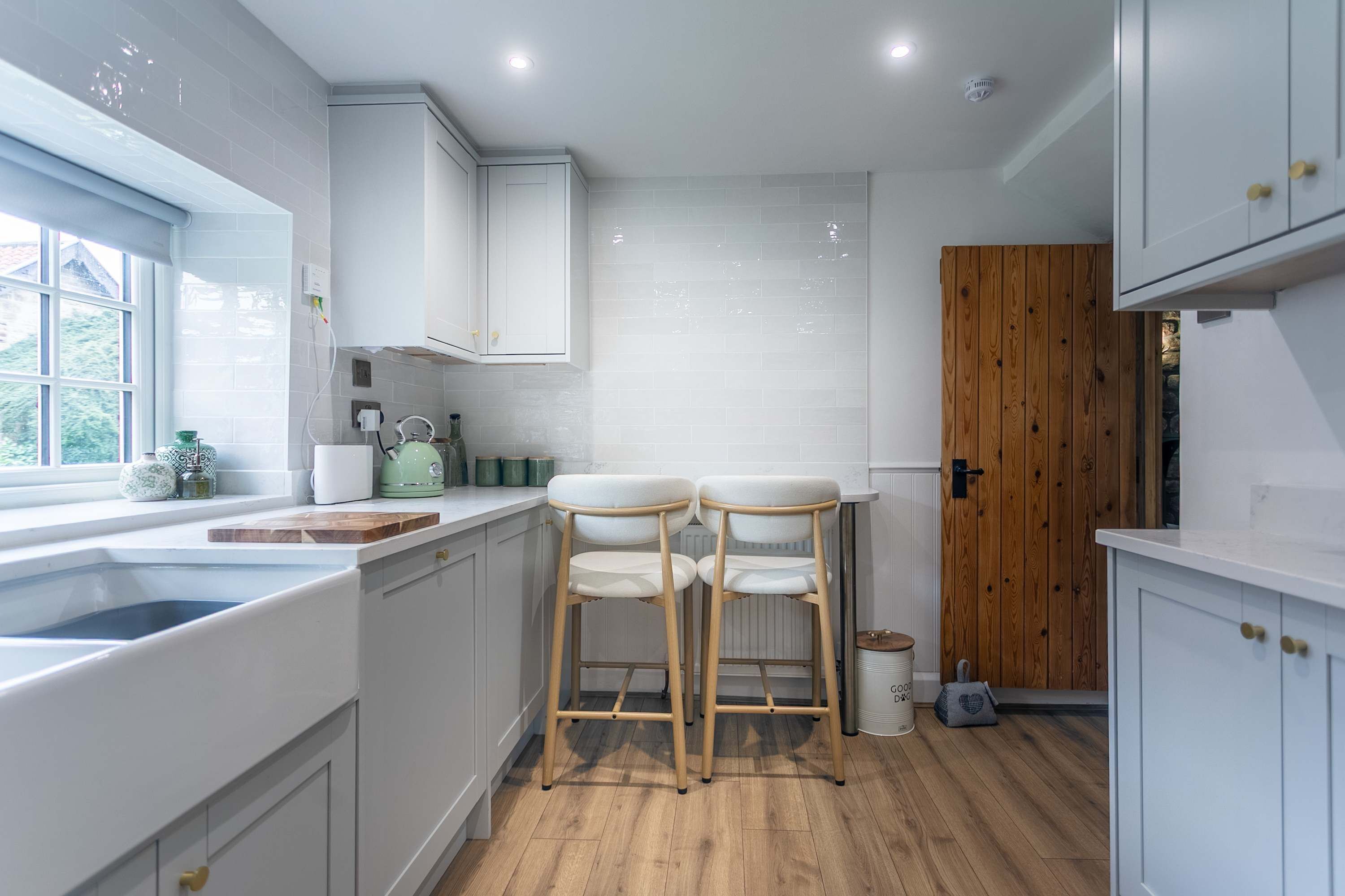Una cucina moderna con mobili bianchi, pavimento in legno e una finestra.