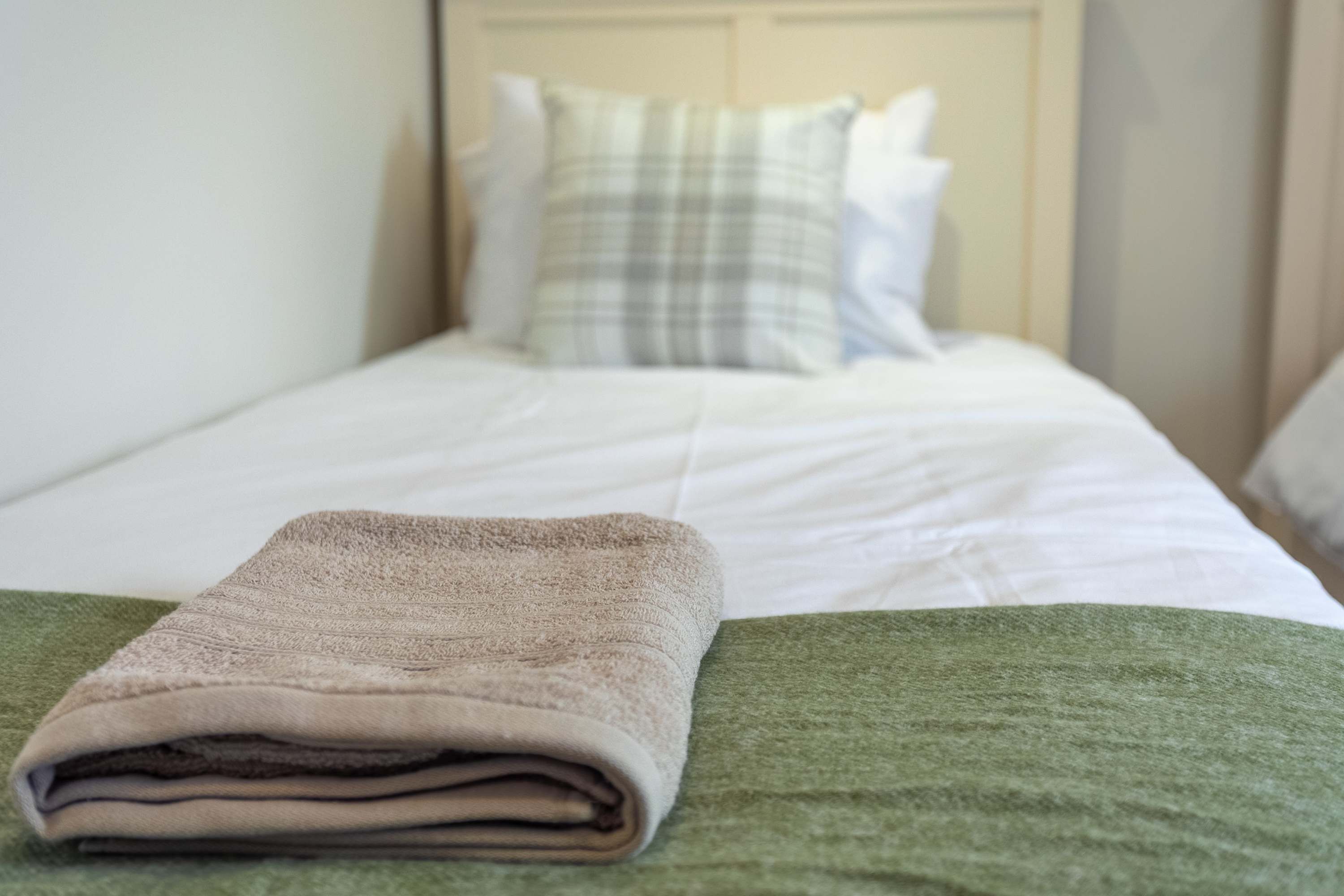 Una cama bien hecha con una toalla doblada al lado.