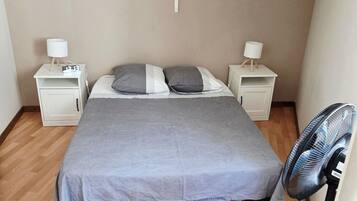 A bedroom with a bed, two bedside tables, a wall-mounted fan, and a decorative wreath.