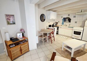 Cocina compacta con armarios blancos, comedor con mesa y sillas, un reloj en la pared y un refrigerador pequeño.