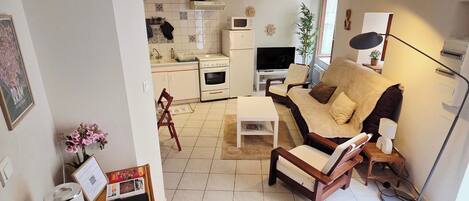 Un salon comprenant un canapé, une table basse et un téléviseur. Il y a également un coin cuisine avec un réfrigérateur, un four à micro-ondes et une cuisinière.