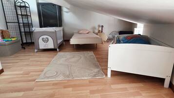 Ein Zimmer mit schrägem Dach, einem Bett, einem Babybett und einem Spielbereich, mit Holzboden.