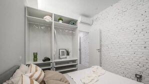 Un dormitorio con una cama, una pared de ladrillo blanco, un armario blanco y una pequeña estantería con una planta.