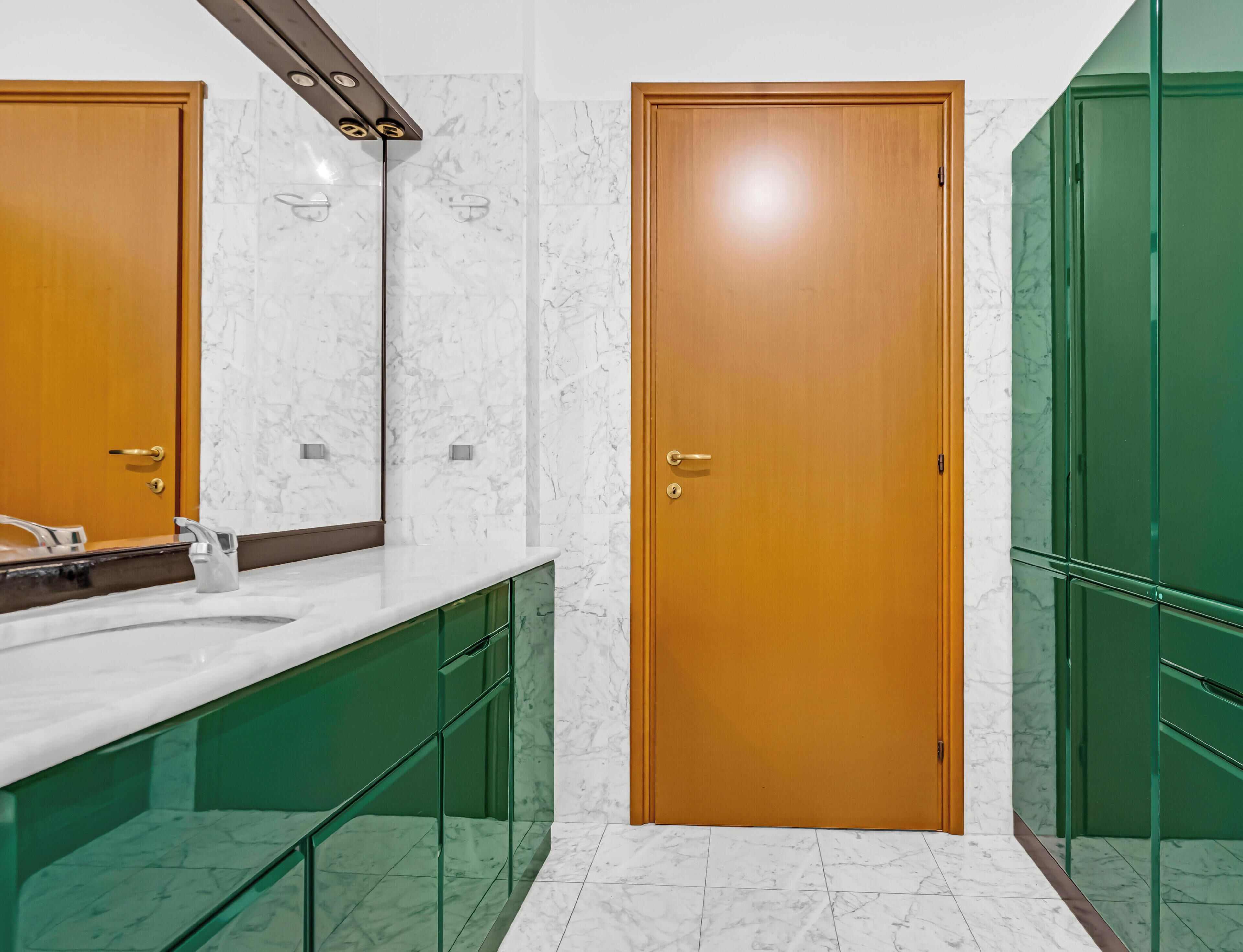 Een badkamer met een houten deur, een spiegel, een wastafel en groene kastjes.