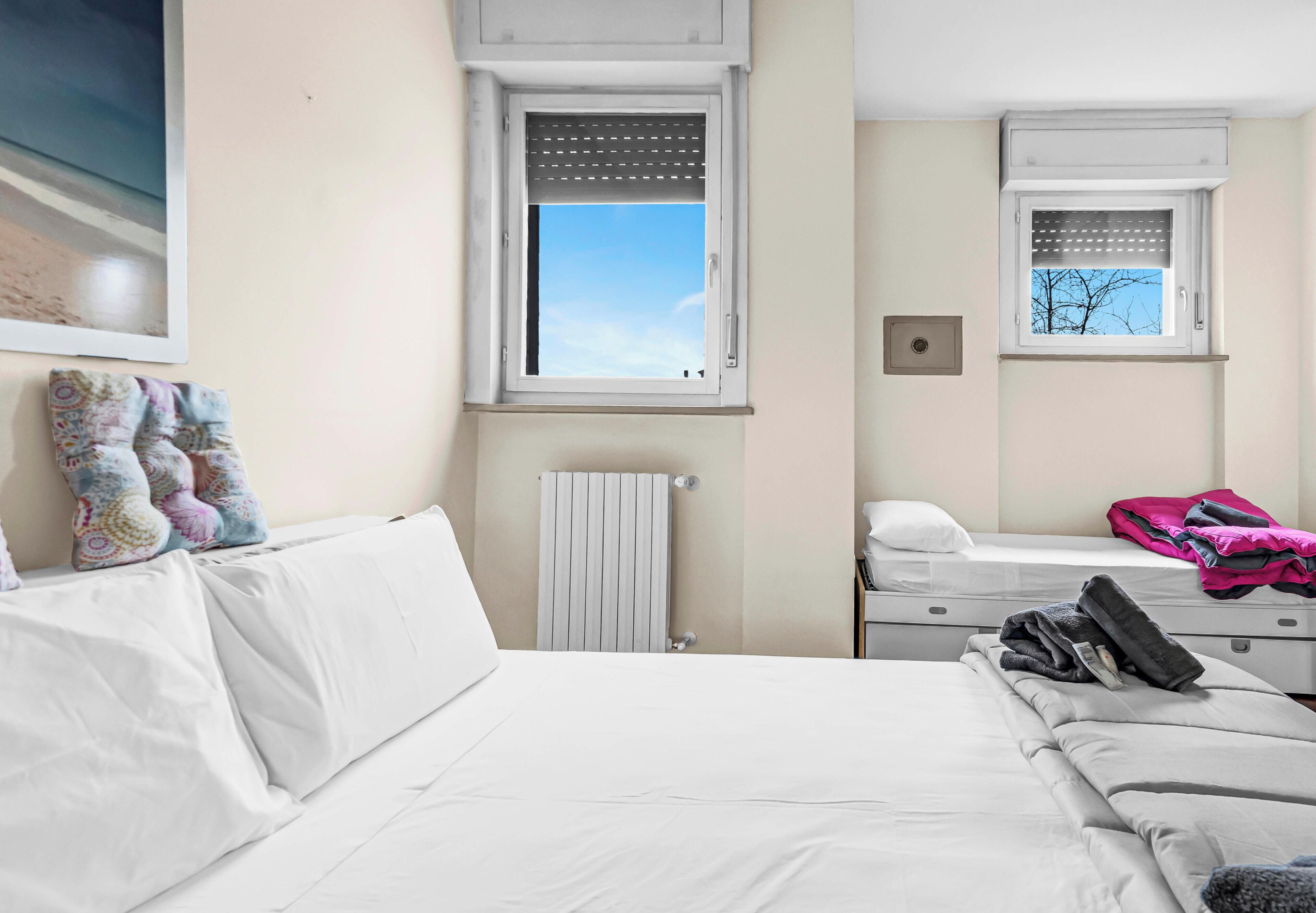 Ein Hotelzimmer mit Bett, Nachttisch, Heizkörper, Fenster und Spiegel.
