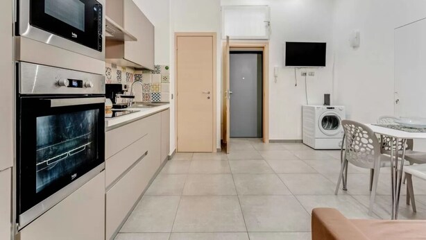 Ett modernt kök med inbyggda vitvaror, en matplats med bord och stolar samt en tvättmaskin.