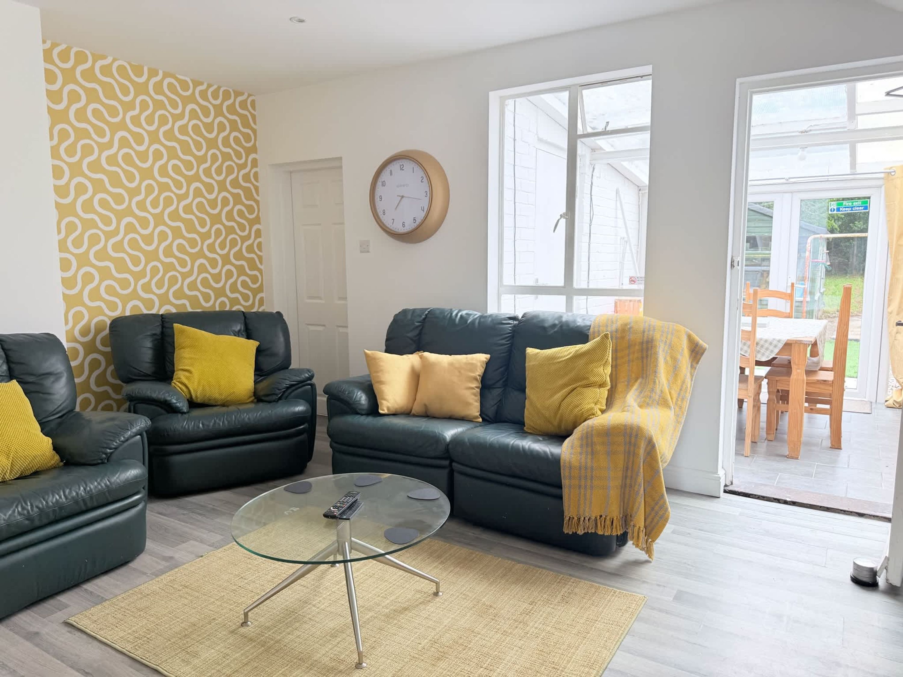 Ein Wohnzimmer mit zwei Ledersofas, einem Glastisch und einer Wand mit Muster.
