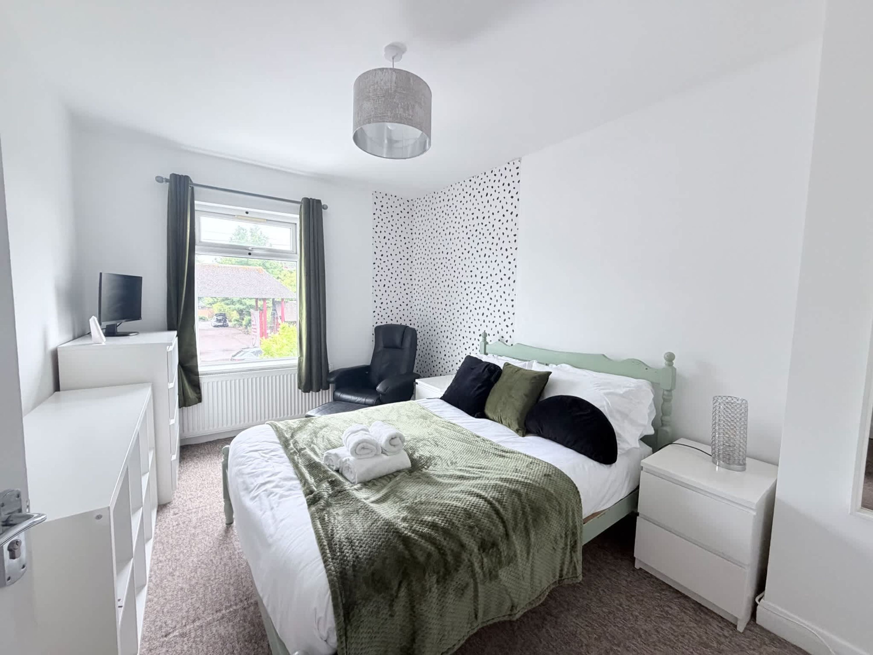 A bedroom with a bed, a desk, a chair, a TV, and a window with curtains.