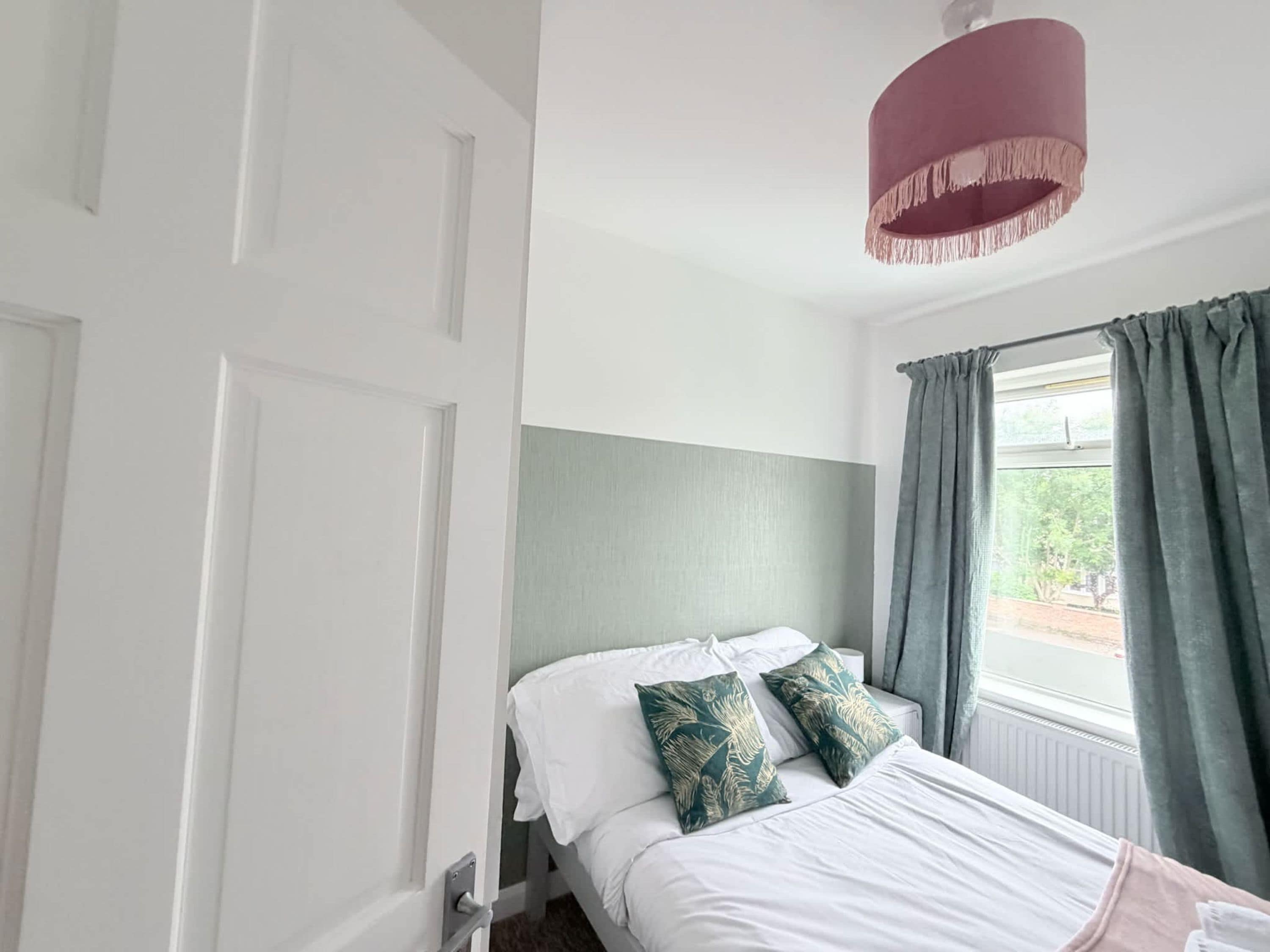 A bedroom with a bed, a window with curtains, a door, and a ceiling light fixture.
