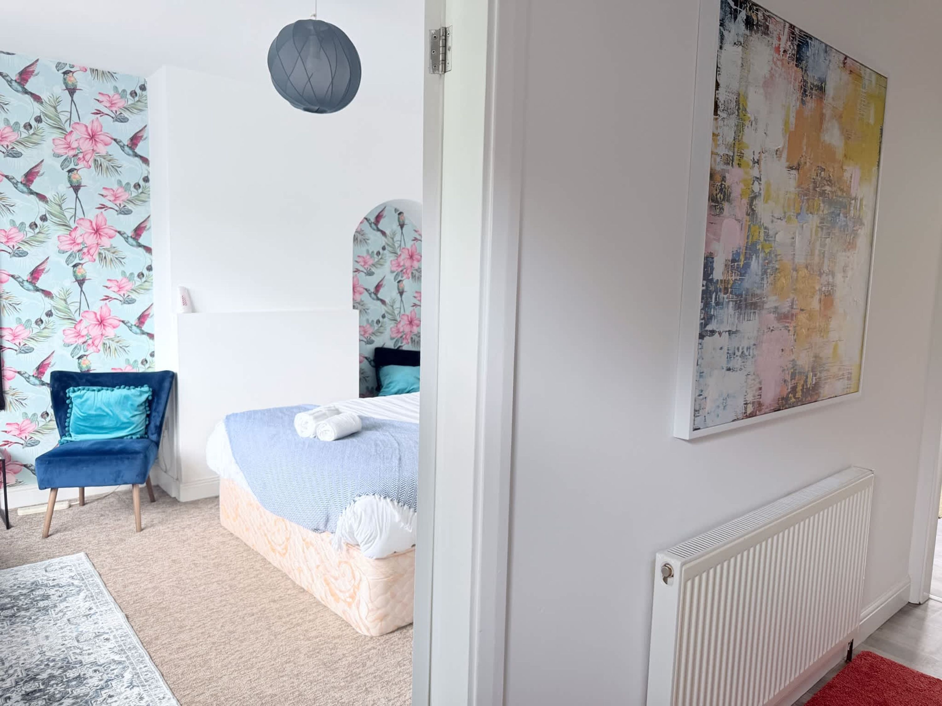 A bedroom with a bed, a chair, a radiator, and a wall with a floral pattern.