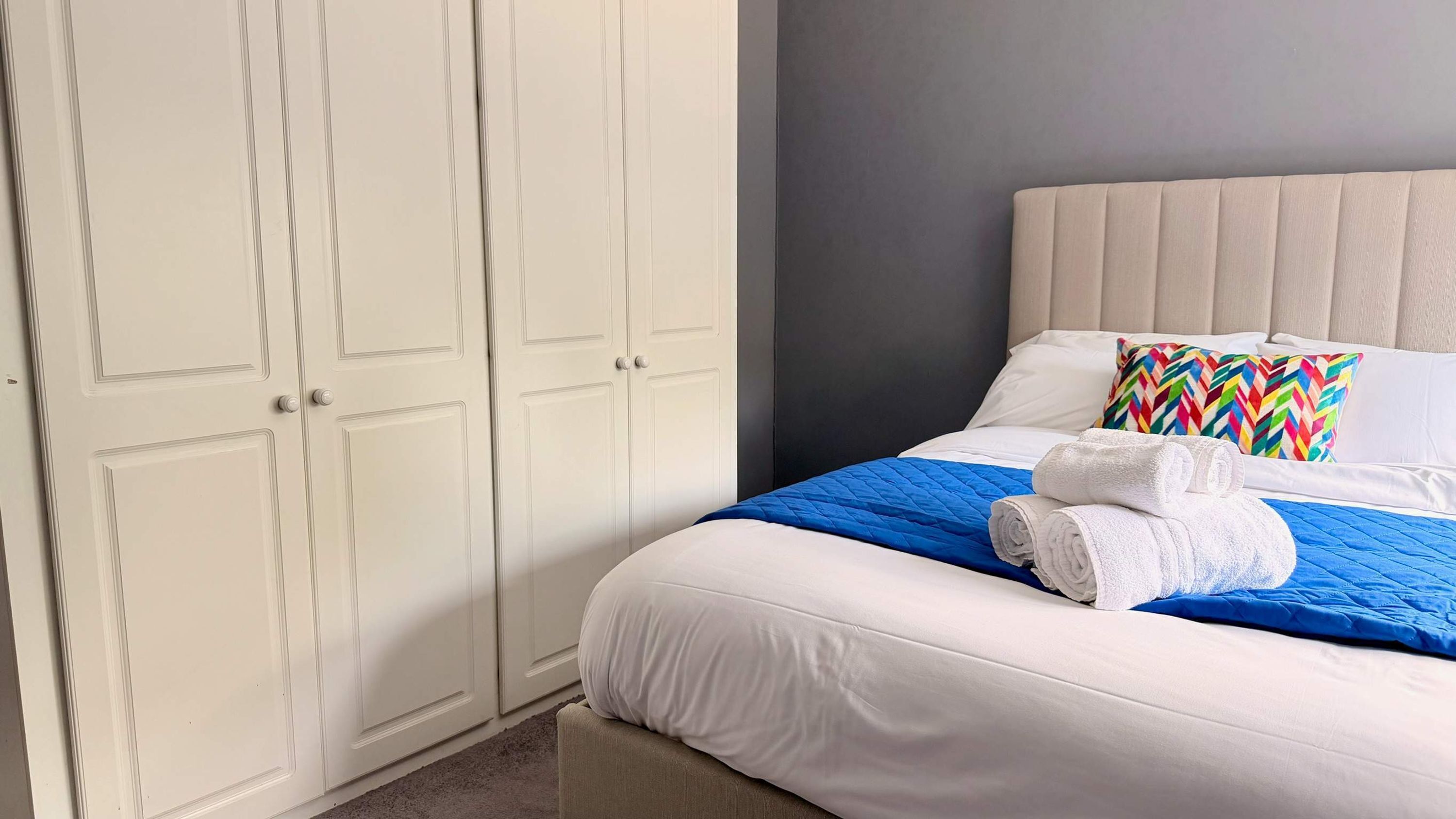 A hotel room with a bed, a wardrobe, and a pillow with a colorful pattern.