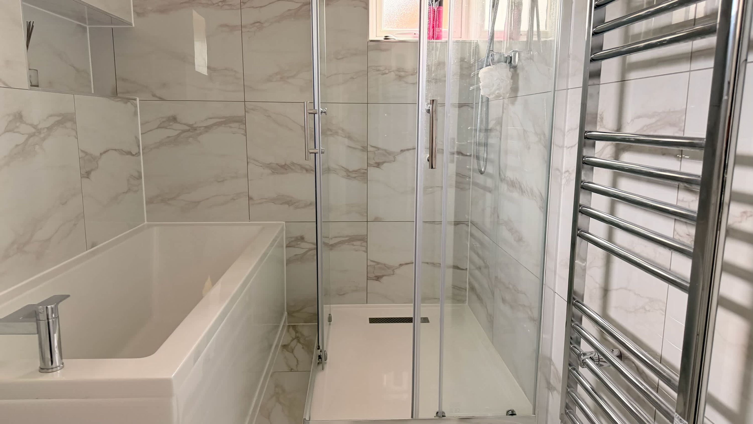 A bathroom with a glass-enclosed shower, a bathtub, and a metal towel rack.
