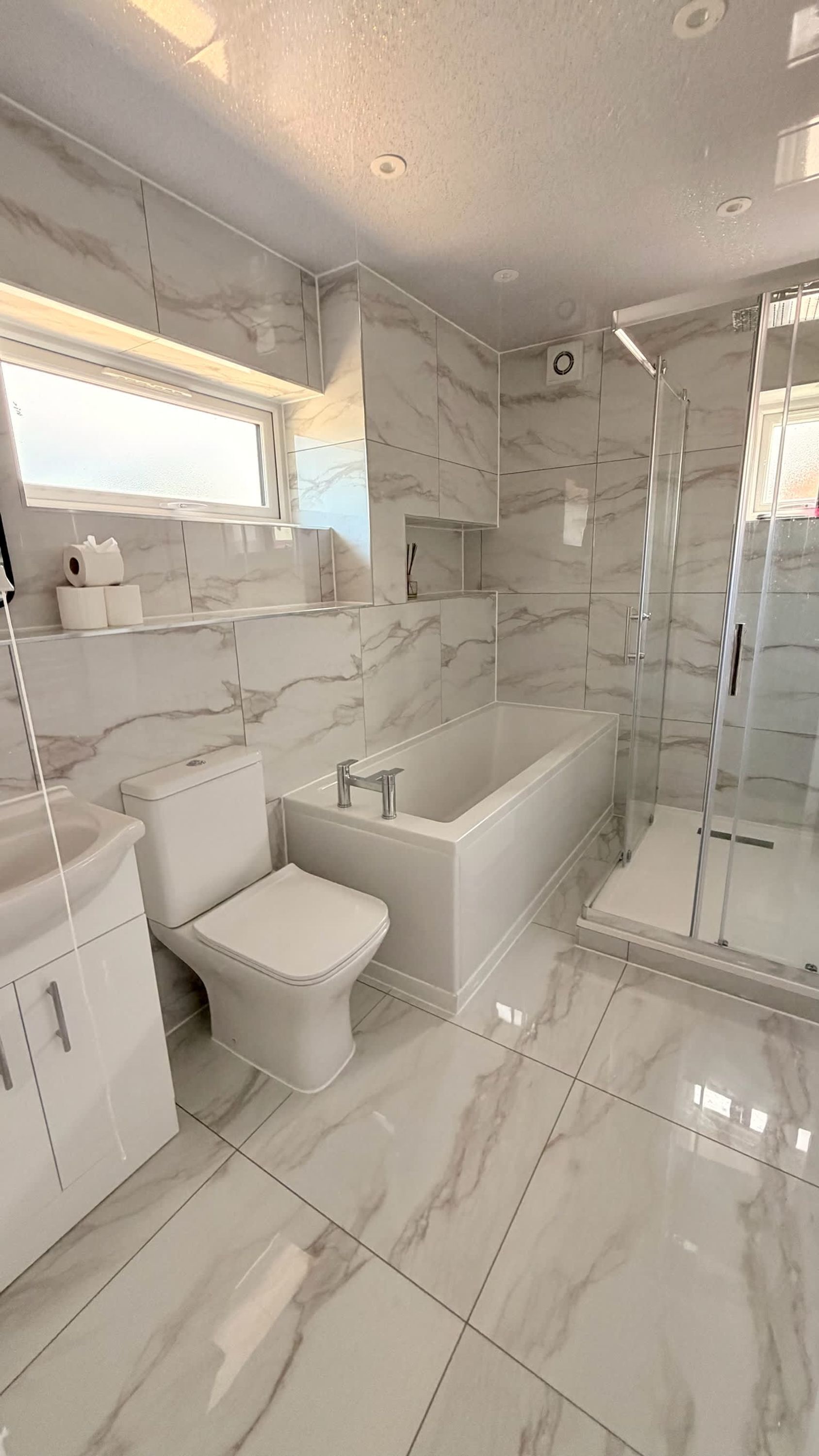 A modern bathroom with a toilet, bidet, bathtub, and glass shower enclosure.