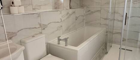 A modern bathroom with a toilet, bidet, bathtub, and glass shower enclosure.