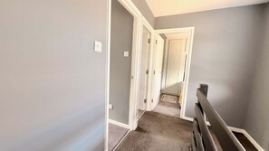 A narrow hallway with a carpeted floor, white trim, and a door at the end.
