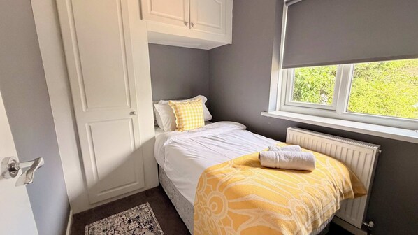 A bedroom with a bed, a window, a radiator, and a door.
