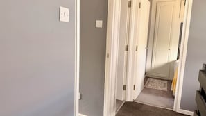 A hallway with a carpeted floor, a door with a white frame, and a light switch on the wall. - Duxford Spacious 4BR Home Near IWM Duxford Aviation (Cambridge)