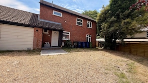 A two-story brick house with a garage, a gravel driveway, and a tree in the yard.