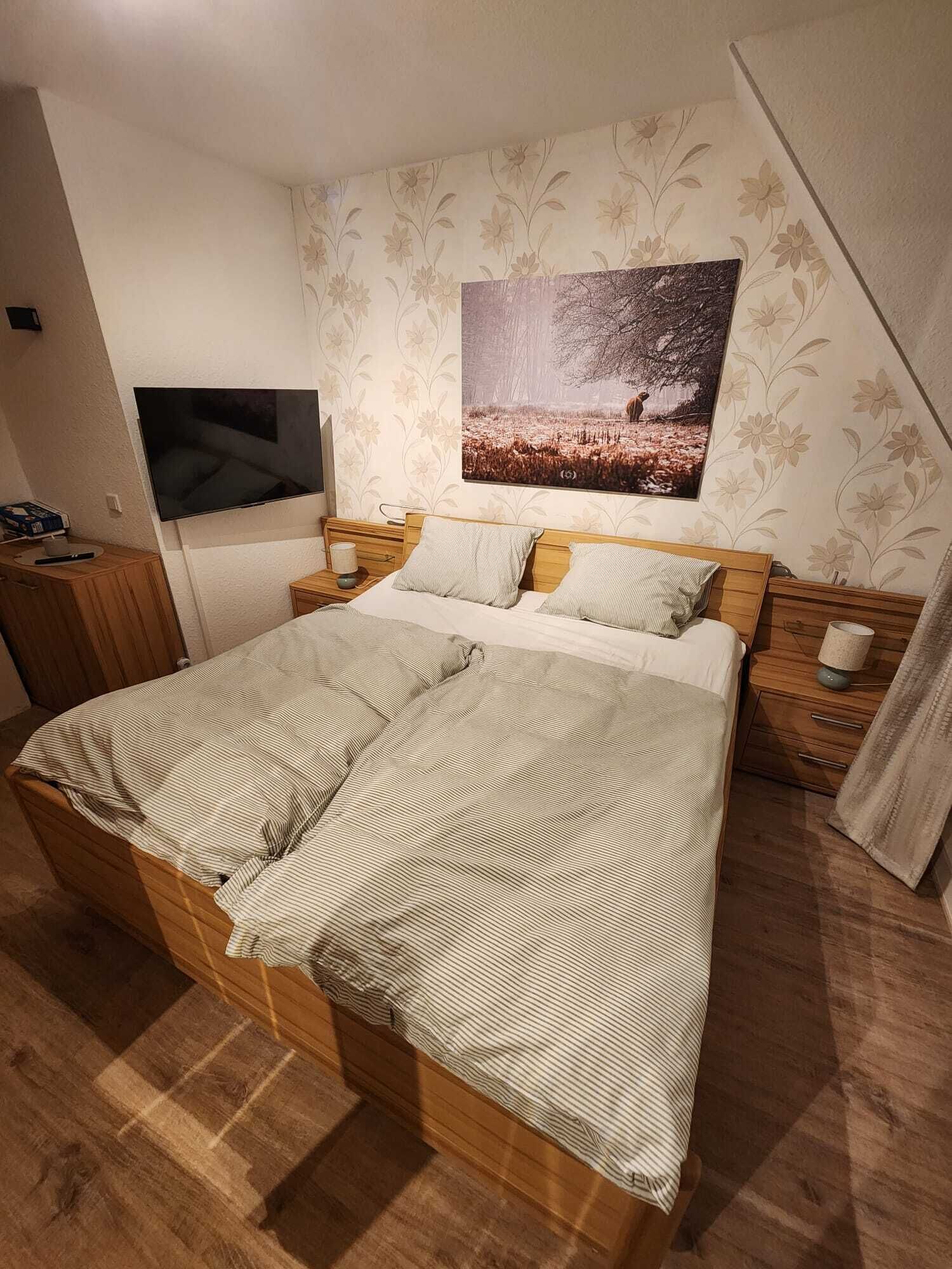 A bedroom with a large bed, a TV mounted on the wall, and a floral wallpaper design.
