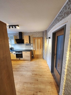 A modern kitchen with a wooden floor, built-in appliances, and a patterned wallpaper.
