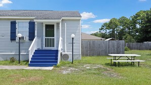 A house with a front porch, a set of stairs, a picnic table, and a wooden fence in the background. - Welcome to The Blue Bungalow! This cozy 2BR/1BA home is the perfect base for a relaxing Emerald Coast getaway, with a full kitchen, in-unit laundry, WiFi, and a quiet backyard just a short drive from Navarre Beach. (Navarre)
