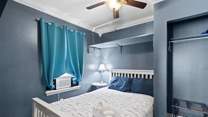 A bedroom with a bed, a window with curtains, a ceiling fan, and a nightstand with a lamp. - Welcome to The Blue Bungalow! This cozy 2BR/1BA home is the perfect base for a relaxing Emerald Coast getaway, with a full kitchen, in-unit laundry, WiFi, and a quiet backyard just a short drive from Navarre Beach. (Navarre)