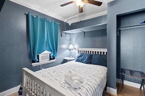 Ein Schlafzimmer mit einem Bett, einem Vorhangfenster, einem Deckenventilator und einem Nachttisch mit Lampe.