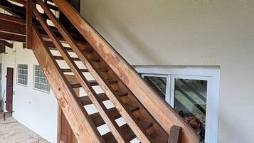 Eine Holztreppe führt zu einem Fenster im zweiten Stock, darunter befinden sich ein Tisch und Stühle.