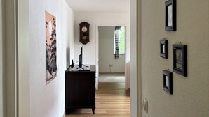Un pasillo con suelo de madera, un aparador de madera oscura, un reloj de pared y varias fotos enmarcadas.