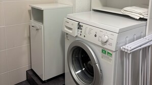 Un lavadero pequeño con lavadora y secadora Bosch, un armario y pared de azulejos.