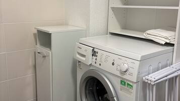 A compact laundry room with a Bosch washing machine and dryer, a small cabinet, and a tiled wall.