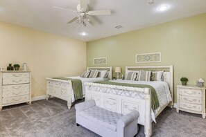 Une chambre avec deux lits, un ventilateur de plafond, une commode et un banc.