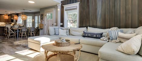A spacious living room with a large sofa, a round wicker coffee table, and a dining area with chairs and a table.