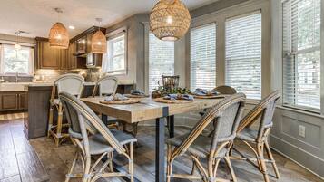 Un espace repas avec une table en bois, des chaises en osier et des luminaires suspendus.