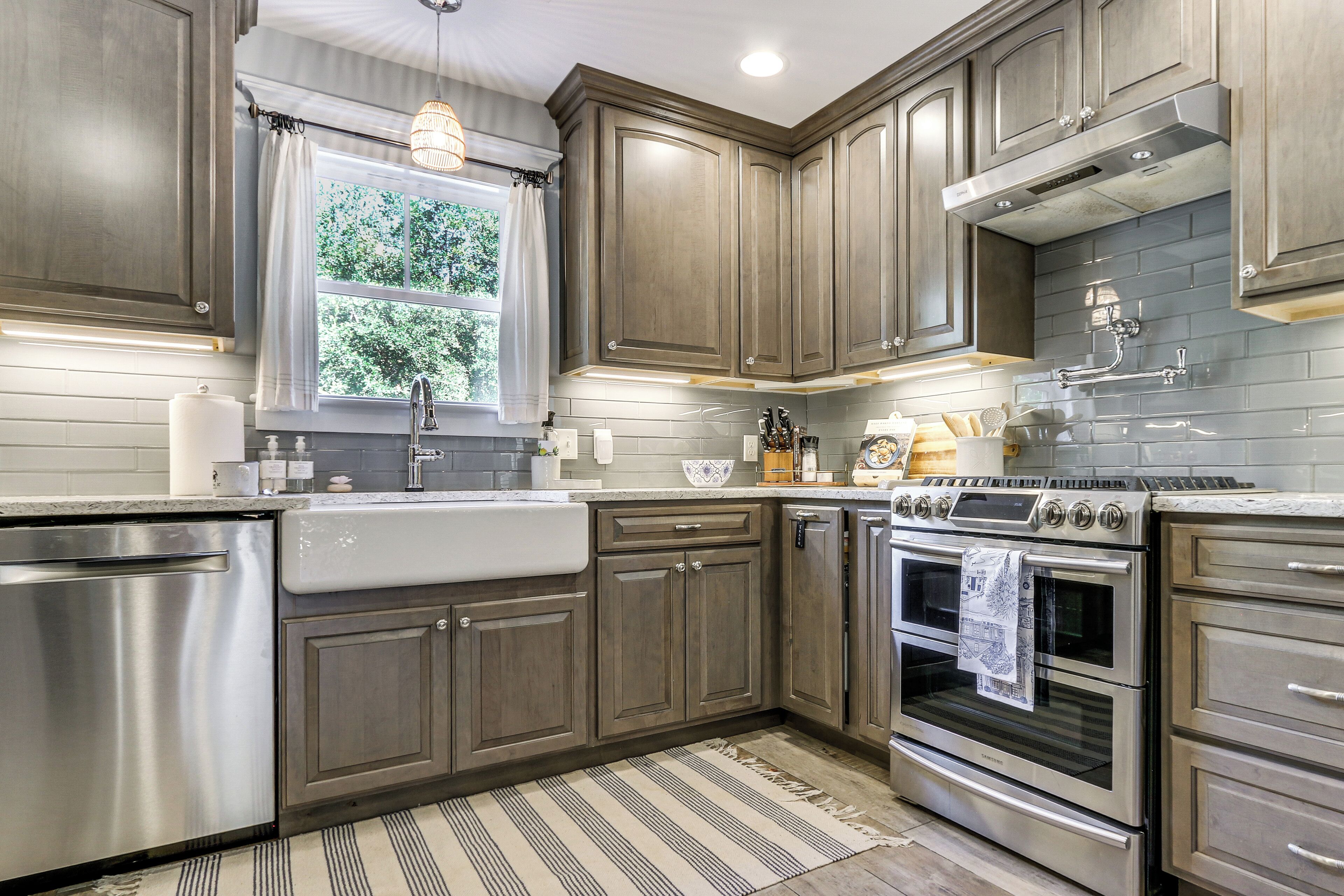 A kitchen with stainless steel appliances, wooden cabinets, and a window with curtains.