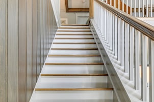 Una escalera con escalones de madera y barandillas blancas, que conduce a un rellano con una pared blanca y un cuadro enmarcado.