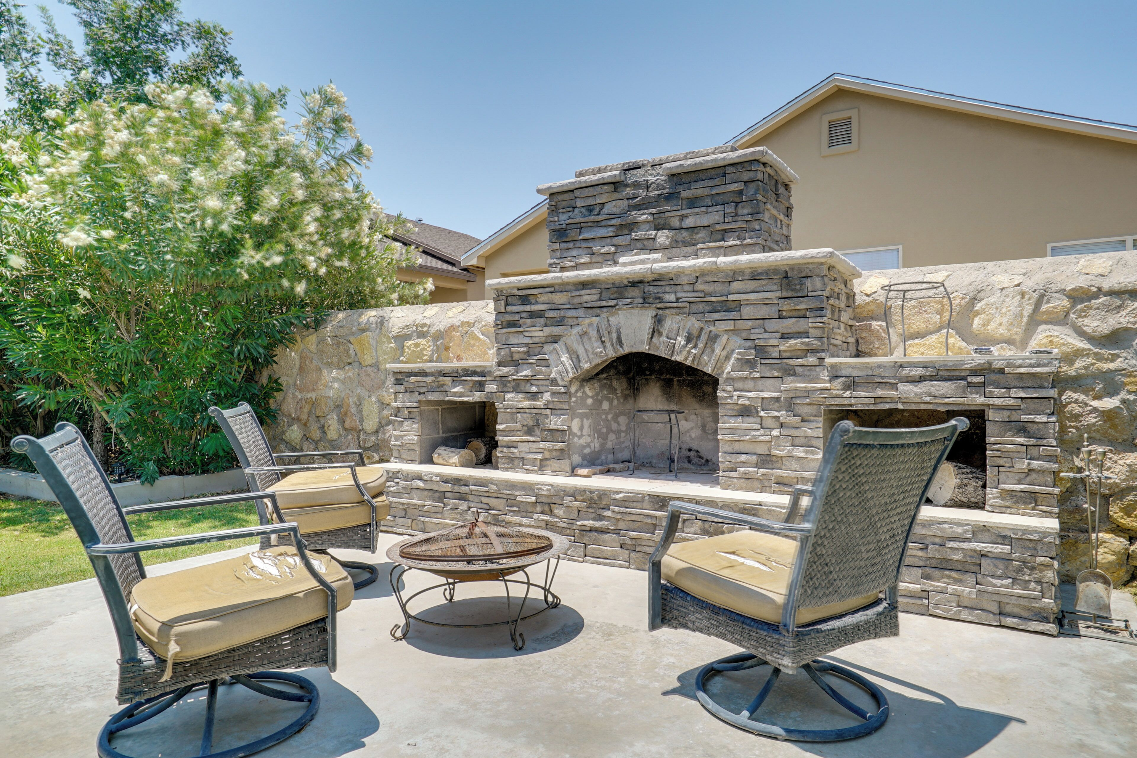 An outdoor patio with stone walls, a stone fireplace, wicker furniture, and a concrete floor.