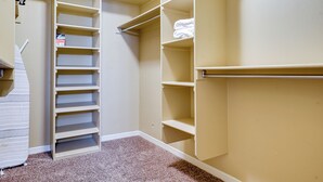 Ein begehbarer Kleiderschrank mit mehreren Regalen und Ablageflächen, ein Teppichboden und eine Tür zu einem anderen Raum.