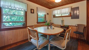 A dining area with a round table, four chairs, and a window with a view of trees. - 3 Mi to Hiking & Beaches: Rustic Maine Cabin (Stockton Springs)