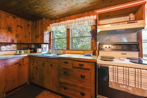 A wooden cabin kitchen with a stove, sink, and cabinets. - 3 Mi to Hiking & Beaches: Rustic Maine Cabin (Stockton Springs)