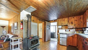 A wooden cabin interior with a wood-burning stove, kitchen area, and a cozy seating area. - 3 Mi to Hiking & Beaches: Rustic Maine Cabin (Stockton Springs)