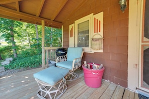 A covered porch with two wicker chairs and a table, a grill, and a pink trash bin. - 3 Mi to Hiking & Beaches: Rustic Maine Cabin (Stockton Springs)