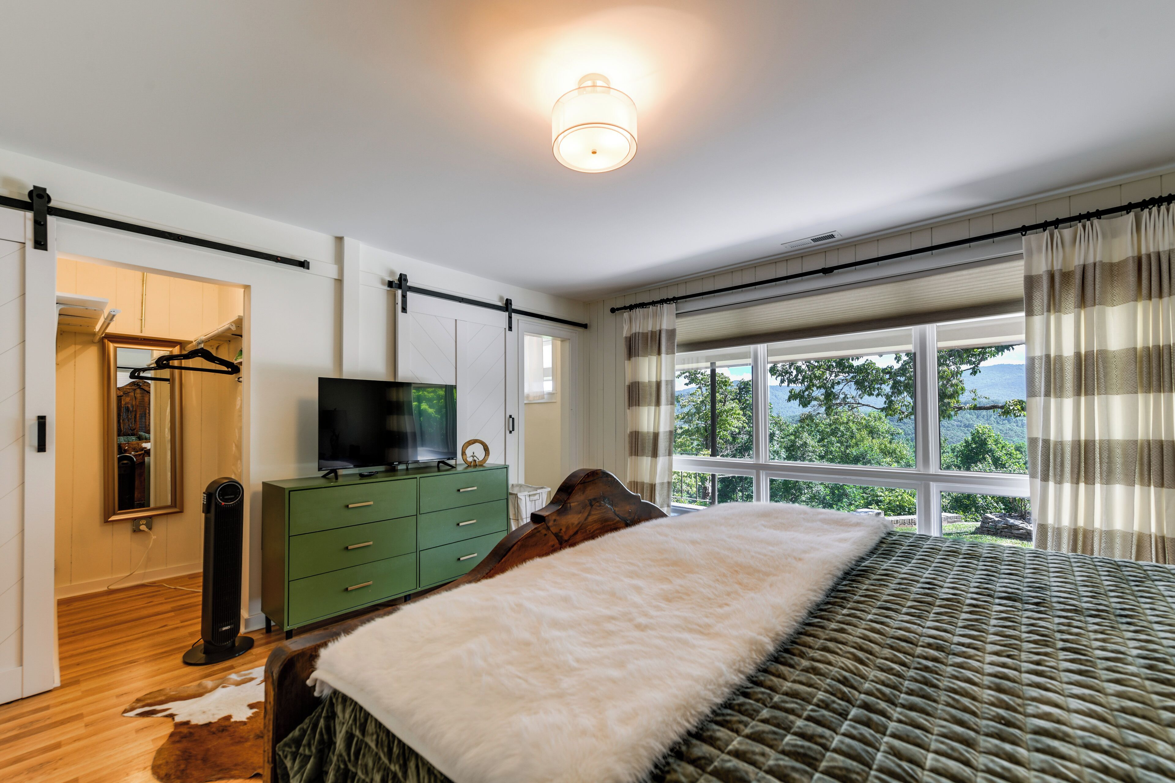 A bedroom with a bed, a dresser, a television, and a window with a view.